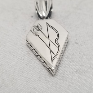 Op de afbeelding: Zilveren hanger met een gedetailleerde gravure van een boog en pijl. De hanger is diamantvormig en heeft een getextureerde rand.