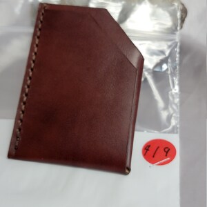 May include: A brown leather card holder with a stitched edge. The card holder is on a white surface with a red circle sticker that says "4/9".