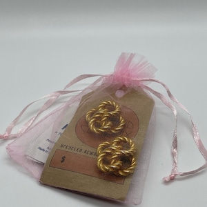 May include: A pair of gold-toned rope knot earrings in a pink organza bag with a brown paper tag that says "Upcycled Rework".