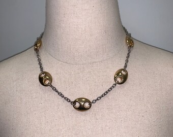 May include: A gold chain necklace with oval-shaped links. The links have a cutout design and are connected by a silver chain.