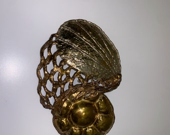 May include: A gold and silver metal wall sculpture with a shell and a flower design.
