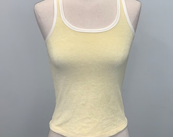 May include: A pale yellow tank top with white trim around the neckline and armholes. The tank top is made of a soft, textured fabric.