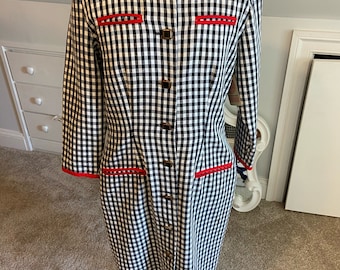 May include: A black and white gingham dress with red trim and button closures. The dress has long sleeves and a knee-length hem.