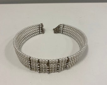 May include: A white pearl choker necklace with a row of clear rhinestones on each side.