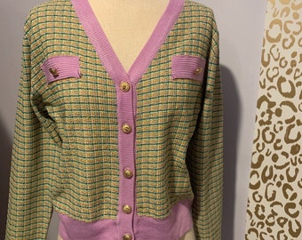 May include: A pink and green checkered cardigan with gold buttons. The cardigan has a v-neck and long sleeves.