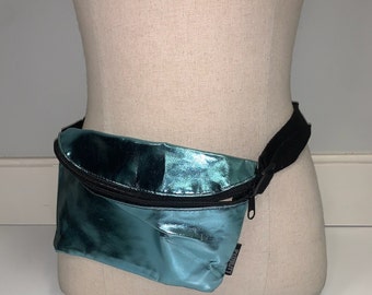 May include: A teal metallic fanny pack with a black zipper and adjustable strap. The pack has a small pocket on the front.