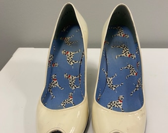 May include: A pair of white peep-toe heels with a dalmatian print lining. The heels are made of patent leather and have a high heel.