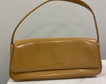 May include: A tan leather handbag with a single top handle and the word "GUESS" embossed on the front.