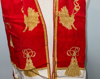 May include: Red silk scarf with a white border and gold tassels. The scarf has a repeating pattern of gold tassels and rope.