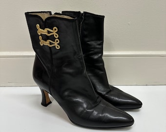 May include: Black leather ankle boots with gold buckle accents and a pointed toe. The boots have a high heel.