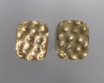 May include: A pair of gold-toned hammered metal earrings. The earrings are square shaped with a textured surface.