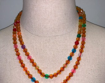 May include: A double strand necklace made of orange, red, green, blue, and clear glass beads. The beads are round and have a faceted finish.