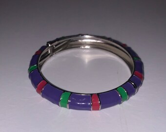 May include: A purple bangle bracelet with red, green, and silver accents. The bracelet is made of metal and has a hinged clasp.