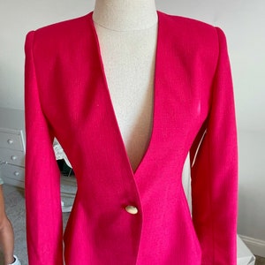 Könnte beinhalten: Ein pinkfarbener Blazer mit einem einzigen goldenen Knopf und einem tiefen V-Ausschnitt.