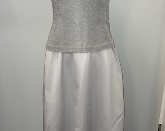 May include: A silver sleeveless top with a v-neckline and a matching white skirt. The top is made of a sparkly fabric and the skirt is made of a smooth satin fabric.