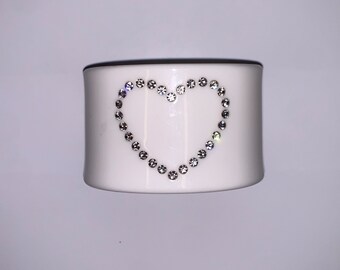 May include: White ceramic napkin ring with a heart design made of clear rhinestones.