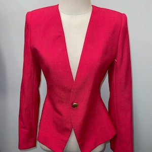 May include: A hot pink blazer with a deep V-neck and a single gold button. The blazer has a fitted silhouette and long sleeves.