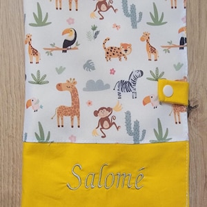 Peut inclure: Une housse de matelas à langer blanche et jaune avec un imprimé d'animaux de safari. La housse présente des girafes, des singes, des zèbres et des toucans. La partie inférieure est jaune avec le nom "Salomé" brodé en cursive.