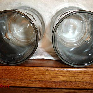 May include: Two clear glass mugs with black rims and handles. The mugs are empty and sitting on a wooden surface.