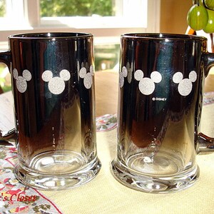 May include: Two black and silver glass beer mugs with a white Mickey Mouse silhouette design. The mugs have a gradient effect, fading from black to silver. The text "&copy;DISNEY" is printed on the bottom of one mug.