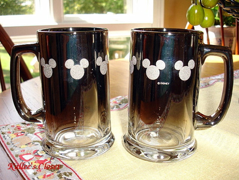 May include: Two black and silver glass beer mugs with a white Mickey Mouse silhouette design. The mugs have a gradient effect, fading from black to silver. The text "&copy;DISNEY" is printed on the bottom of one mug.