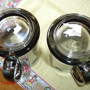 May include: Two clear glass mugs with black rims and handles. The mugs are empty and have a sticker on the bottom of each.