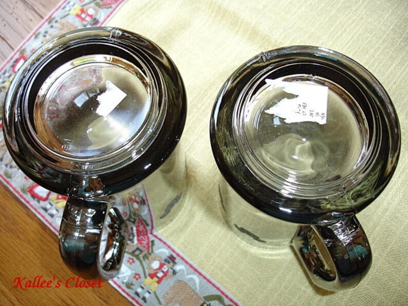 May include: Two clear glass mugs with black rims and handles. The mugs are empty and have a sticker on the bottom of each.