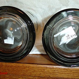 May include: Two clear glass beer mugs with a black rim and a textured surface. The mugs are empty and have a sticker on the bottom.
