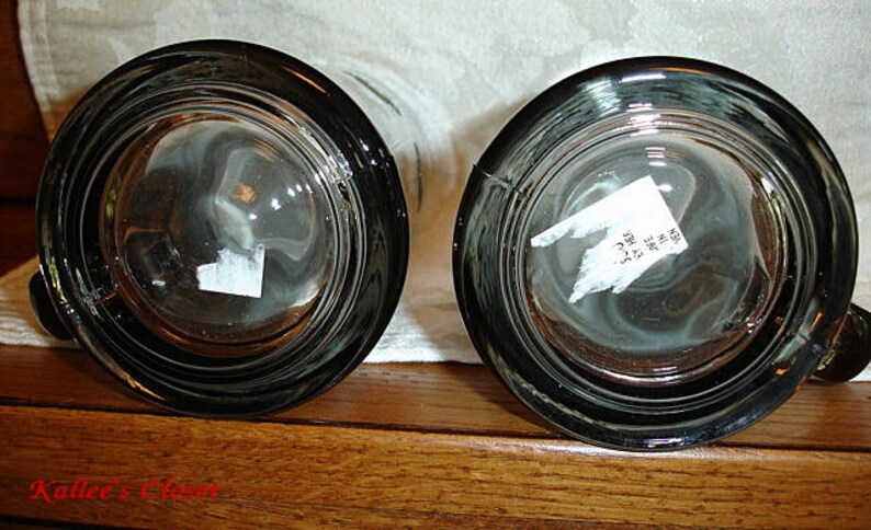 May include: Two clear glass beer mugs with a black rim and a textured surface. The mugs are empty and have a sticker on the bottom.