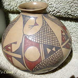 May include: A brown ceramic pot with a geometric design in black and red. The pot has a rounded body and a narrow opening.