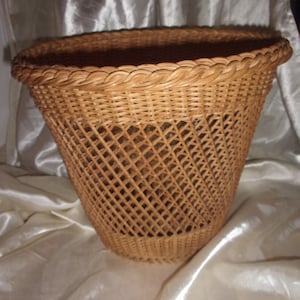 Puede incluir: Una cesta de mimbre marrón con una parte superior ancha y redonda y un patrón tejido. La cesta está hecha de materiales naturales y tiene un aspecto rústico y vintage.