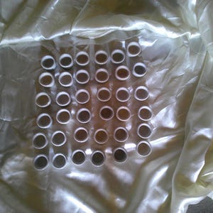 Può includere: Uno sfondo in tessuto bianco con una griglia di 36 piccole tazze in ceramica bianca disposte in sei file di sei tazze ciascuna.