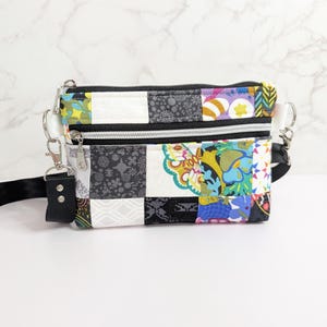 May include: A patchwork crossbody bag with a black adjustable strap. The bag features a variety of colorful fabric squares, including floral and geometric patterns. It has two zippered compartments and silver-tone hardware.