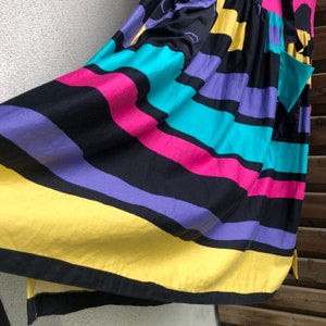Pu&ograve; includere: Un abito colorato con strisce orizzontali nere, viola, rosa, turchese e gialle. L'abito ha una vestibilit&agrave; ampia e una tasca laterale. Il tessuto sembra leggero, adatto ai climi caldi.