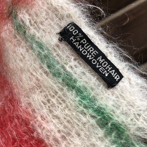 May include: A close-up of a white, red and green striped mohair sweater with a black tag that reads "100% Pure Mohair Handwoven".