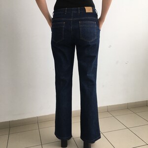 May include: Dark blue denim jeans with a straight leg fit. The jeans have a classic five-pocket style and a button closure.