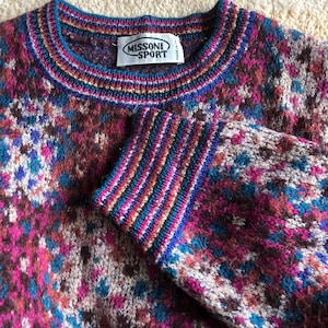 May include: A multi-colored knitted sweater with a geometric pattern. The sweater has a crew neck and a label that reads "Missoni Sport" with "Made in Italy" printed on it.