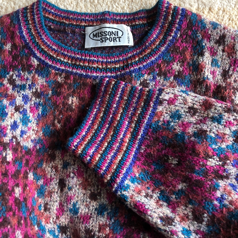 May include: A multi-colored knitted sweater with a geometric pattern. The sweater has a crew neck and a label that reads "Missoni Sport" with "Made in Italy" printed on it.