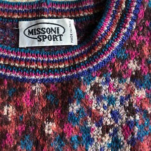 May include: A close-up of a colorful knitted sweater with a Missoni Sport label. The sweater has a brown, pink, blue, and white pattern.