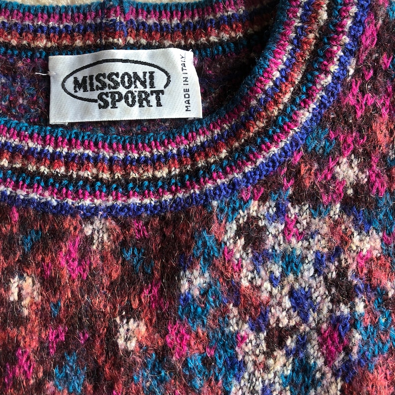 May include: A close-up of a colorful knitted sweater with a Missoni Sport label. The sweater has a brown, pink, blue, and white pattern.