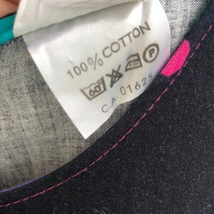 Pu&ograve; includere: Un'etichetta bianca con la scritta "100% COTTON" e simboli di cura. L'etichetta &egrave; cucita su un tessuto nero con cuciture rosa. L'etichetta ha anche il numero "C.A. 01625".