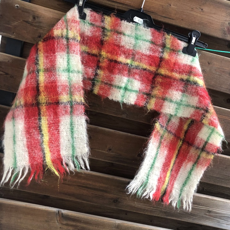 May include: A red, yellow, green and white plaid scarf with frayed edges. The scarf is made of a soft, fuzzy material.