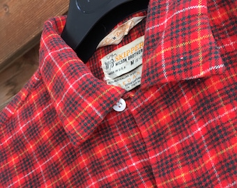 May include: Red and black plaid flannel shirt with a white label that reads "Skipper Wilson Brother" and "Made in U.S.A."