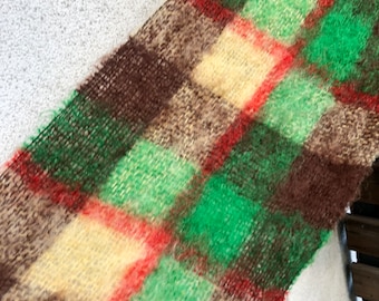May include: A close-up of a plaid fabric with brown, green, red, and cream colored squares. The fabric has a fuzzy texture.