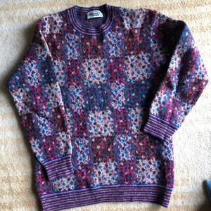 May include: A multi-colored sweater with a geometric pattern in shades of purple, blue, brown, and white. The sweater has a crew neck and ribbed cuffs and hem. The label on the sweater reads "Worsted Sport".