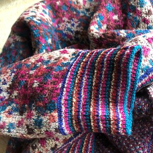 May include: A close-up of a knitted sweater with a colorful, geometric pattern. The sweater is made of a soft, fuzzy yarn and has a ribbed cuff.