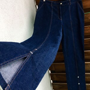 May include: A pair of dark blue denim jeans with a slit on the front of each leg. The jeans have a straight leg and a high waist.