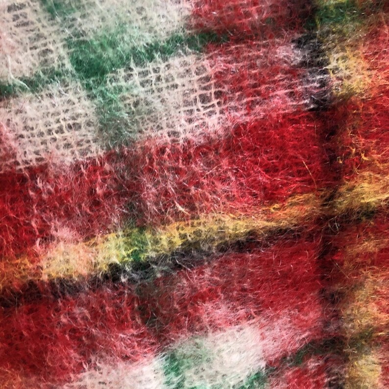 May include: Close-up of a fuzzy plaid fabric with red, green, white and yellow stripes. The fabric has a soft, textured appearance.