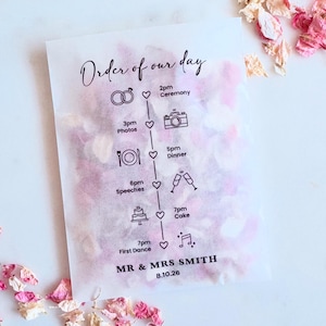 Puede incluir: Una bolsa de papel translúcido llena de pétalos de flores rosas. La bolsa presenta el texto "Order of our day" y un programa de boda con iconos para la ceremonia, fotos, cena, discursos, tarta y primer baile. Los nombres "MR & MRS SMITH" y la fecha "8.10.26" están impresos.