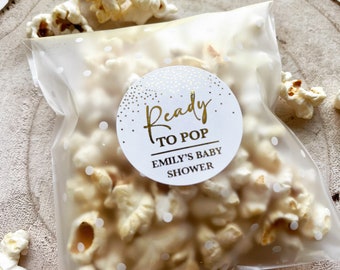 May include: A clear plastic bag filled with popcorn and a white circle sticker with gold lettering that reads "Ready to Pop Emily's Baby Shower".